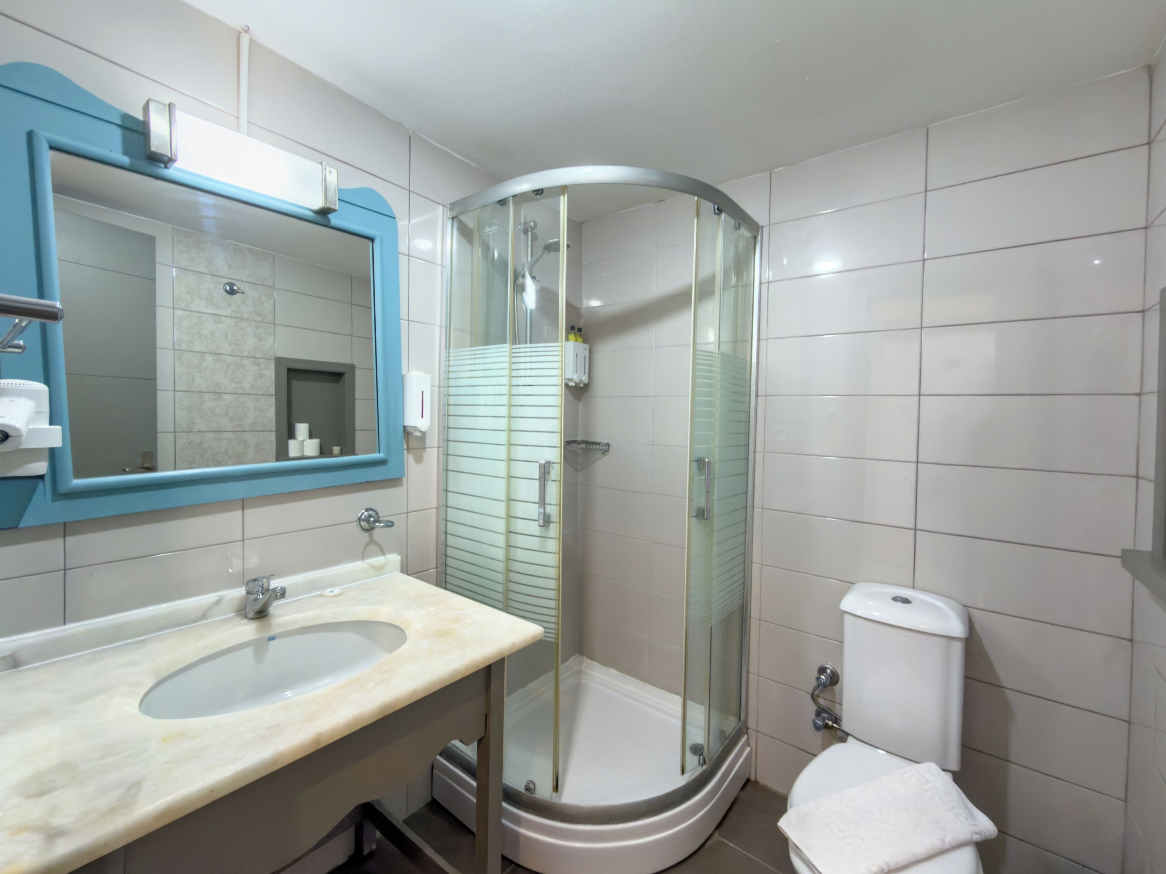 A bathroom with a curved glass shower enclosure, a sink with a marble countertop, and a toilet.
