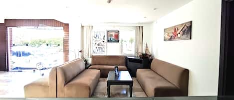 Un salon avec un ensemble de canapés marron, une table basse et une fenêtre donnant sur des voitures garées et sur la verdure à l’extérieur.