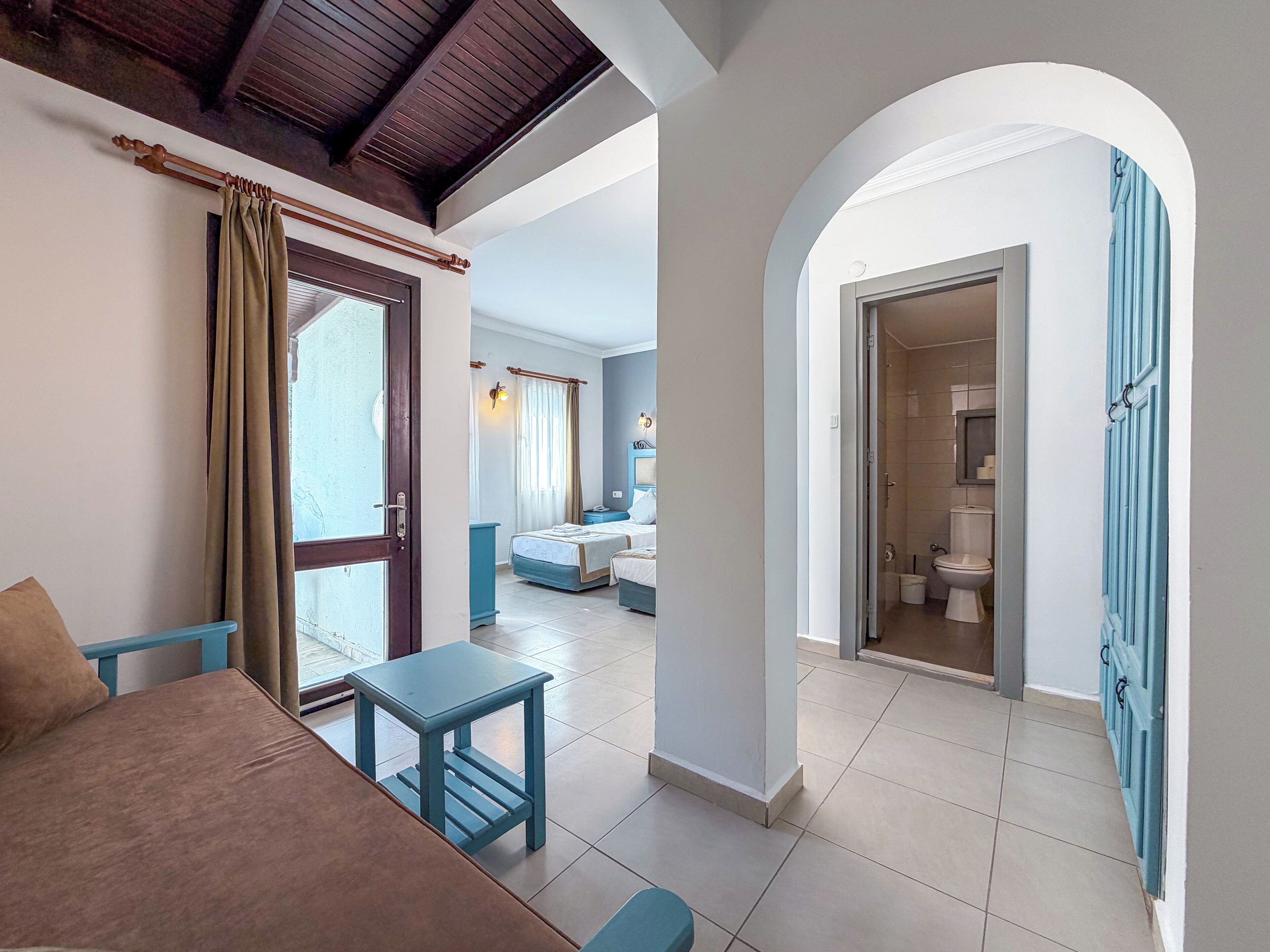 A room with a bed, a small table, a sofa, and a bathroom visible through an archway.