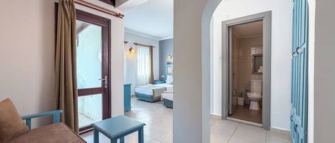A room with a bed, a small table, a sofa, and a bathroom visible through an archway.