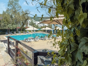 A swimming pool with lounge chairs and umbrellas, surrounded by greenery and buildings.