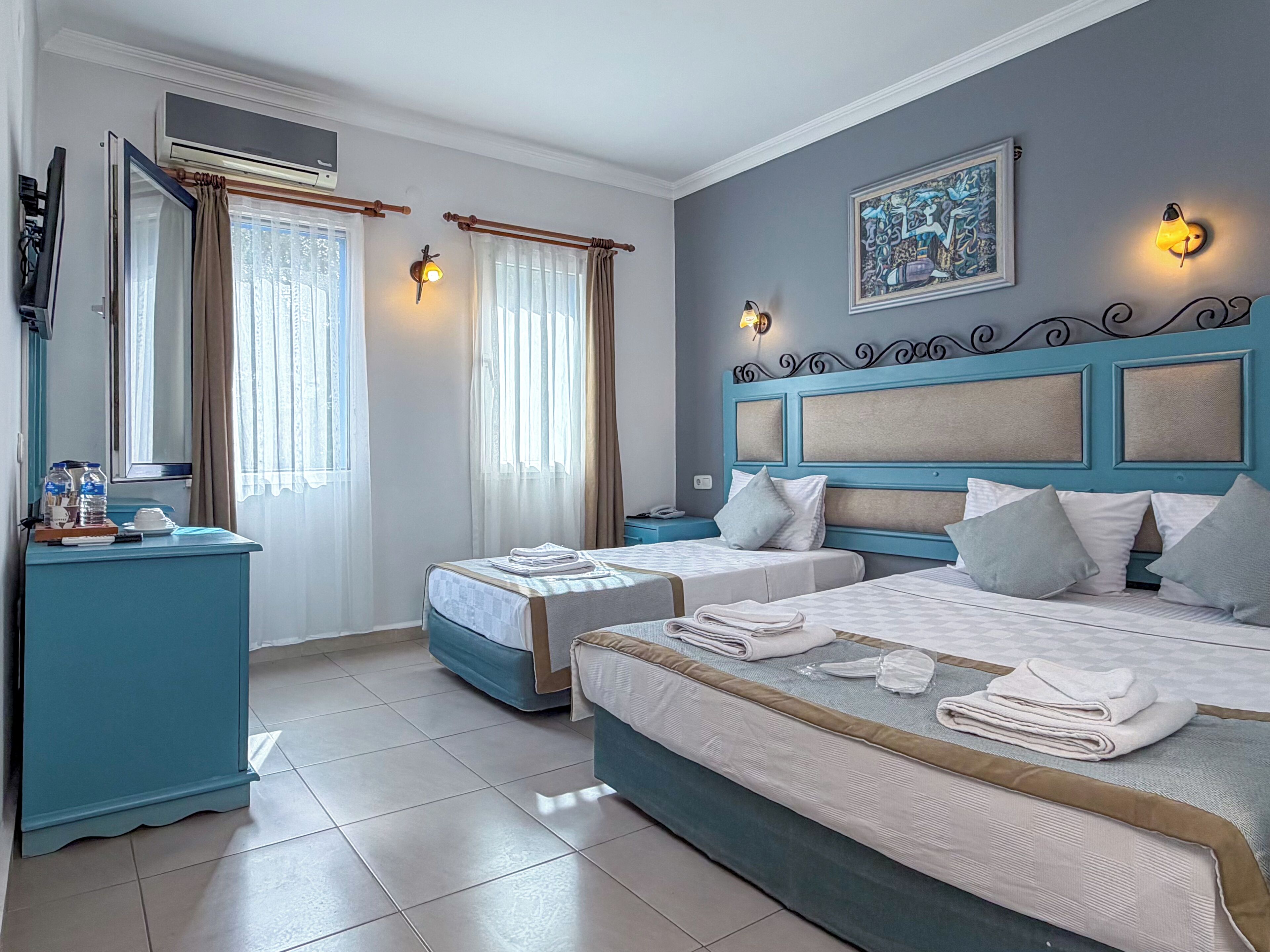 Una habitación de hotel con dos camas, un escritorio, una silla, un equipo de aire acondicionado y un cuadro en la pared.