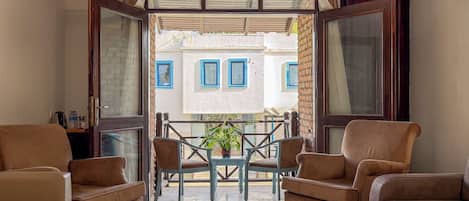 A room with a balcony, two sofas, a table with chairs, and a potted plant.