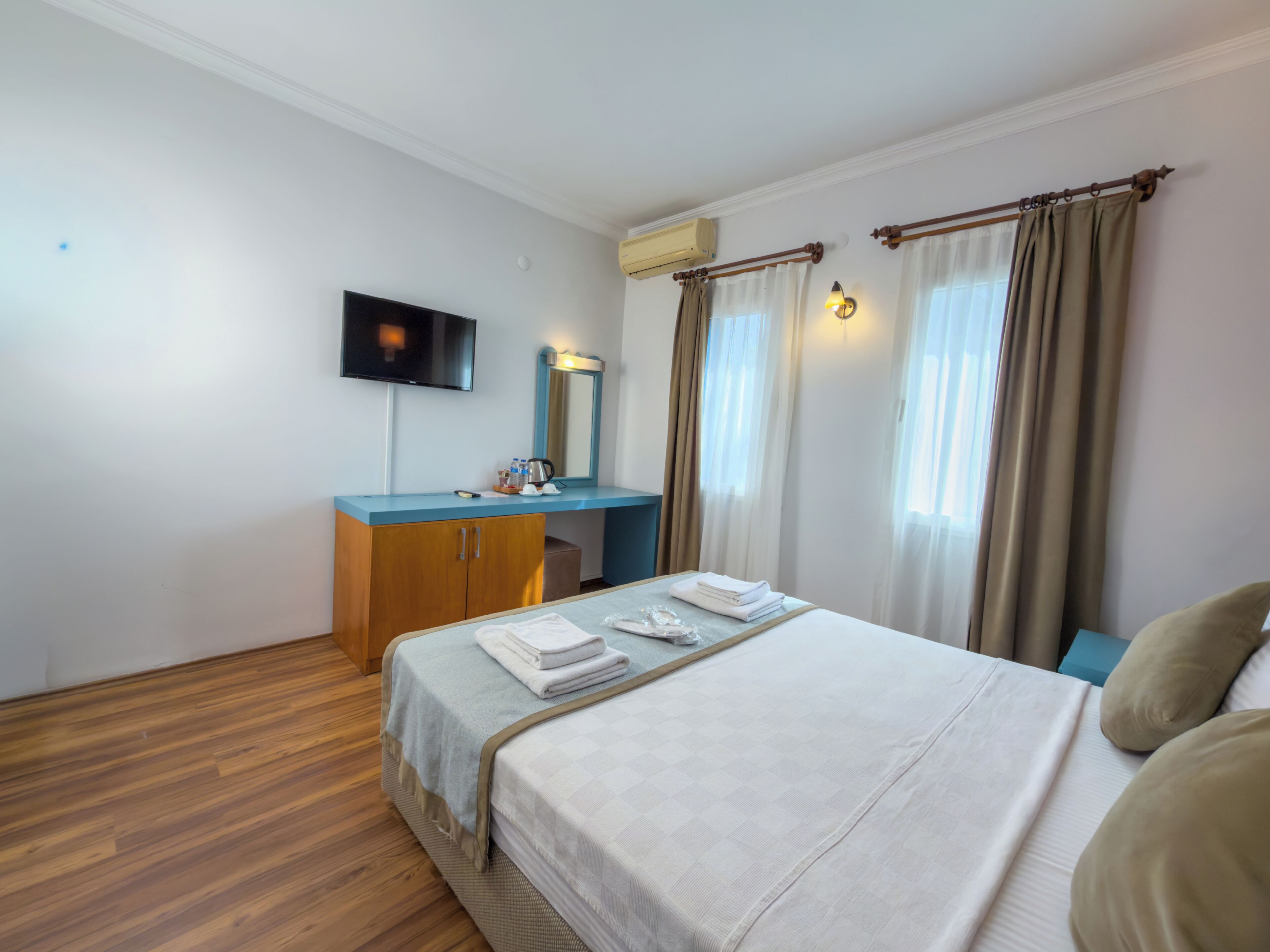 A hotel room with a bed, a desk with a mirror, a television, and a window with curtains.