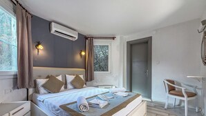 Un dormitorio con cama, mesitas de noche, escritorio, silla, aire acondicionado y ventana con cortinas.
