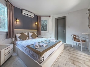 Un dormitorio con cama, mesitas de noche, escritorio, silla, aire acondicionado y ventana con cortinas.