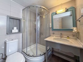 Un baño con ducha de vidrio, un inodoro, un lavabo con espejo y un estante con papel higiénico.