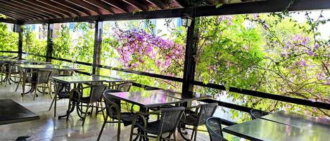 Un espacio al aire libre con mesas y sillas, rodeado de exuberante vegetación y plantas florecientes.