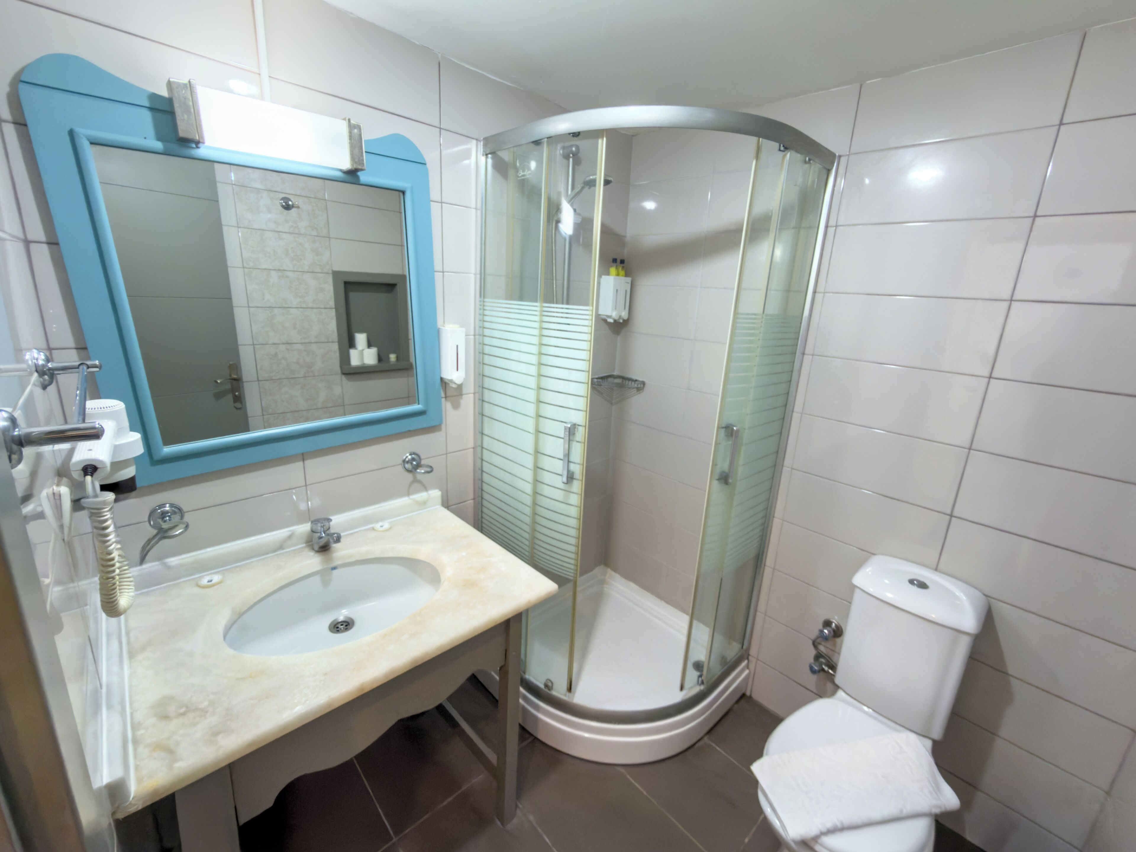 Une salle de bain dotée d’une douche à parois courbes en verre, d’un lavabo avec un plan de toilette en marbre et de toilettes.