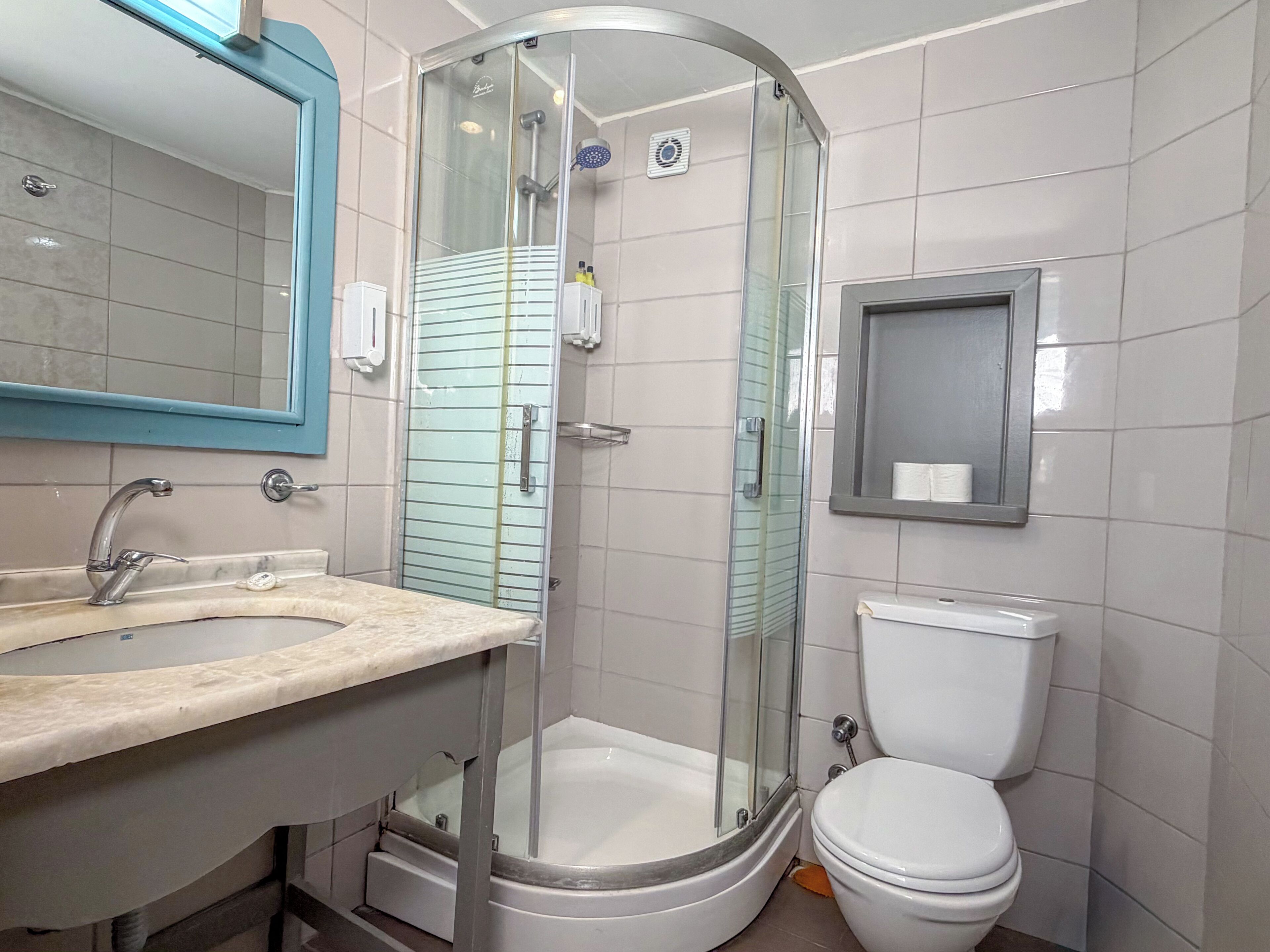 Un bany amb dutxa envidriada, un lavabo amb mirall i un vàter.