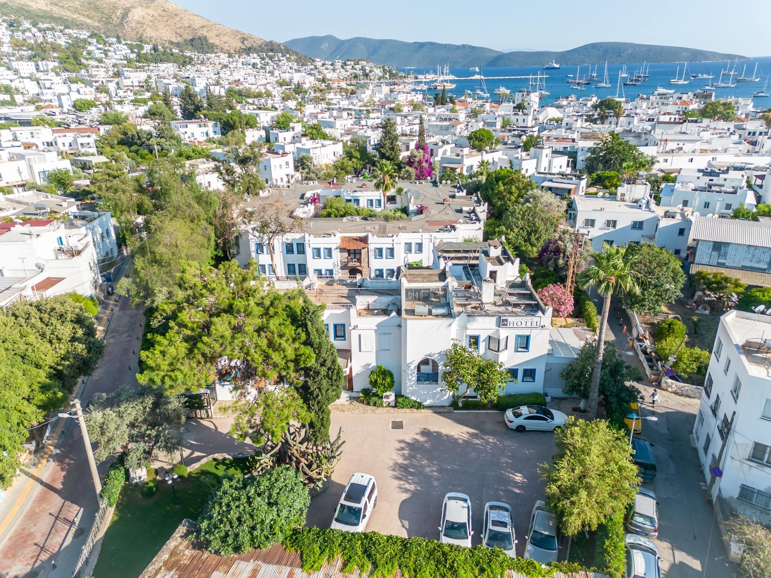 An aerial view of a coastal town with white buildings, a marina with sailboats, and a hotel with a sign.