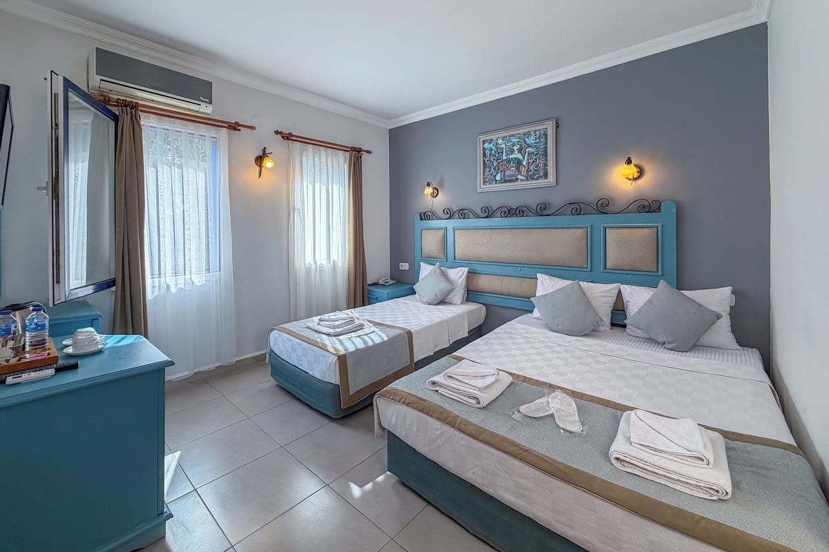 A hotel room with two beds, a desk, a chair, a window with curtains, and a wall-mounted air conditioner.