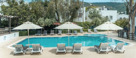 Une piscine entourée d’arbres et de bâtiments, avec des chaises longues et des parasols.