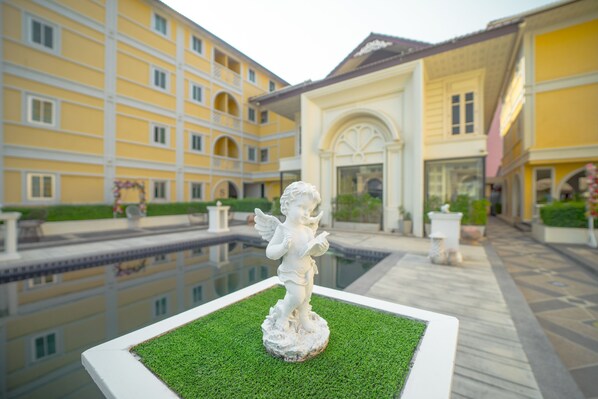 A statue of a cherub on a square platform with a pool in the background.