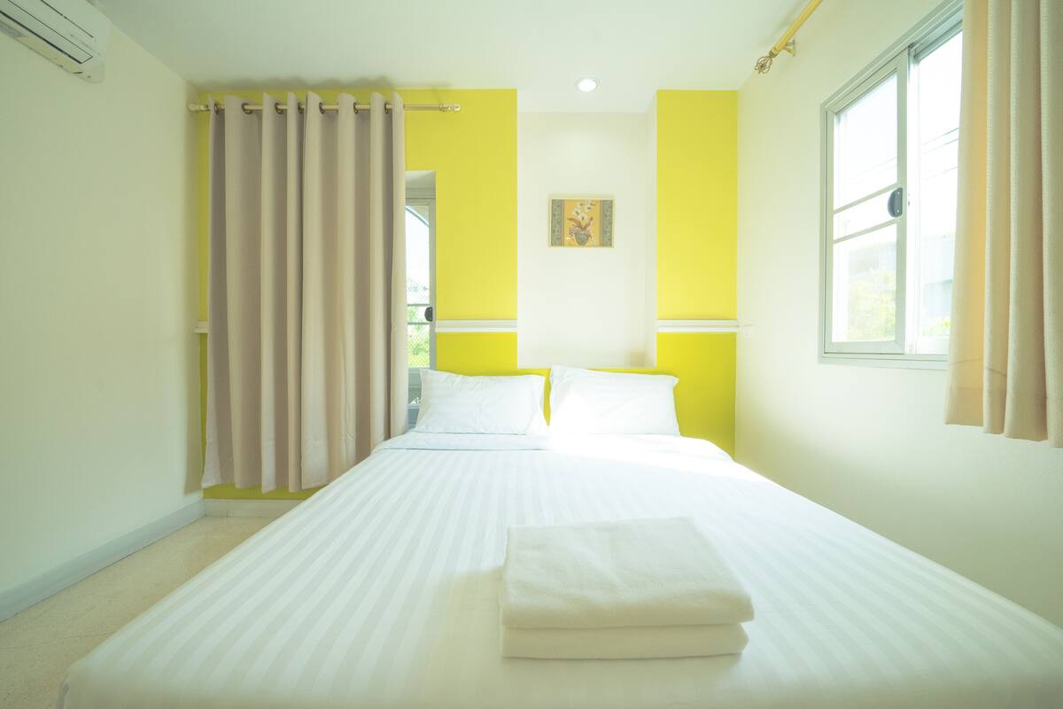 A hotel room with a bed, curtains, a window, and a painting on the wall.