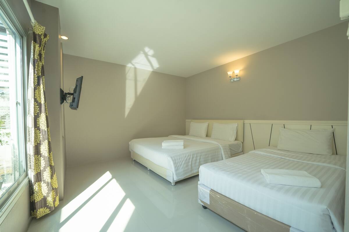 A hotel room with two beds, a window with curtains, a wall-mounted TV, and a ceiling light.