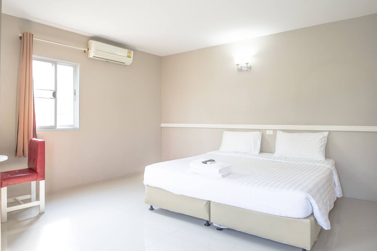 A hotel room with a bed, a chair, a window, and an air conditioning unit.