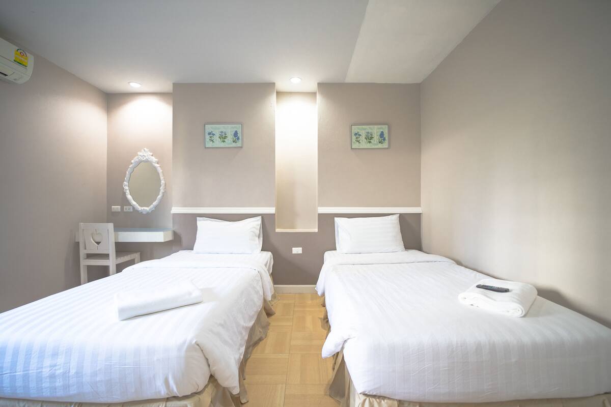 A hotel room with two single beds, a small desk, a chair, and a mirror on the wall.