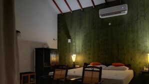 Une chambre avec un lit, deux chaises, une table de chevet, une lampe et un climatiseur.
