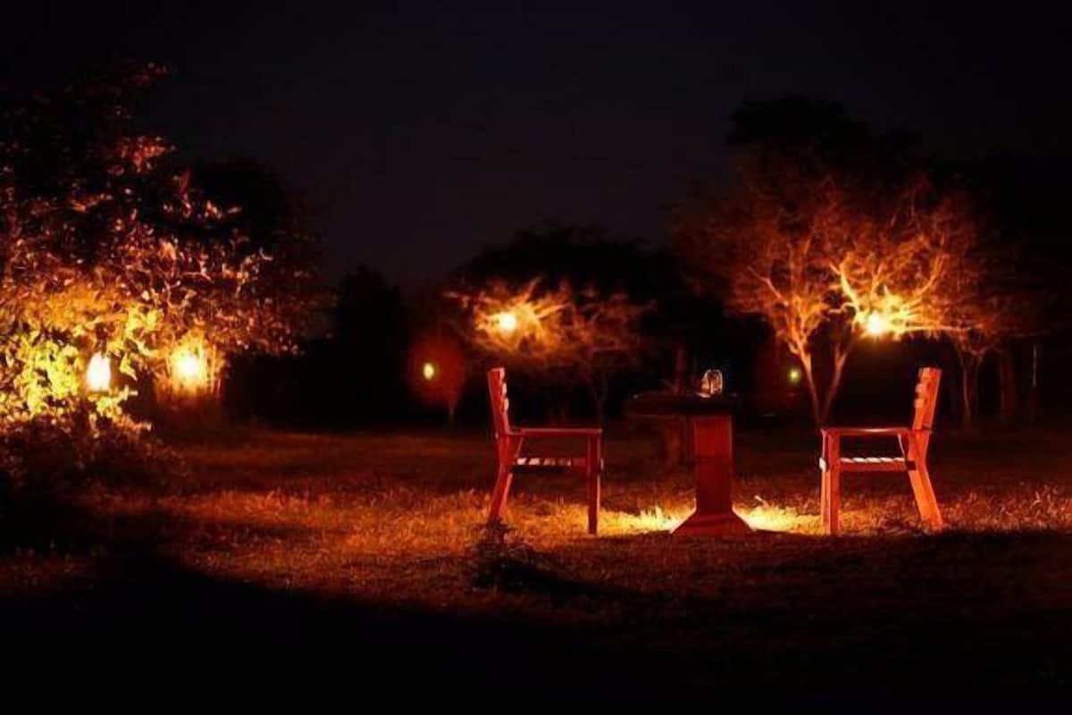 Un área de estar al aire libre con dos sillas y una mesa, rodeada de árboles e iluminada por luces cálidas.