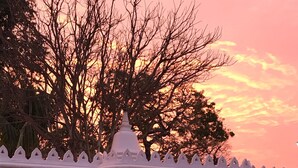 Un temple se dressant sur fond de ciel rosâtre, avec une entrée blanche et deux statues.