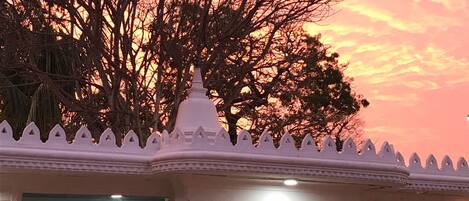 Un templo con un cielo rosado al fondo, una entrada blanca y dos estatuas.