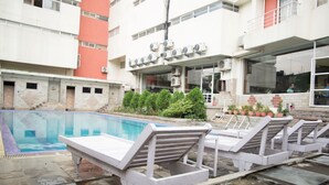 A swimming pool with lounge chairs, a building with air conditioning units, and a staircase leading to an upper level. - Hotel Samana (Hetauda)