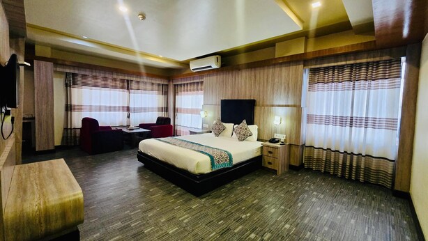 A hotel room with a large bed, a desk with a chair, a TV, and a bedside table with a lamp. - Hotel Samana (Hetauda)