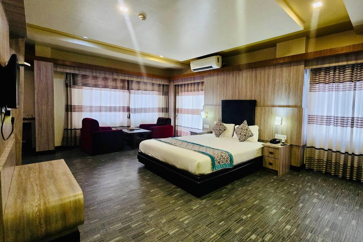 Ein Hotelzimmer mit einem großen Bett, einem Schreibtisch mit Stuhl, einem Fernseher und einem Nachttisch mit Lampe.