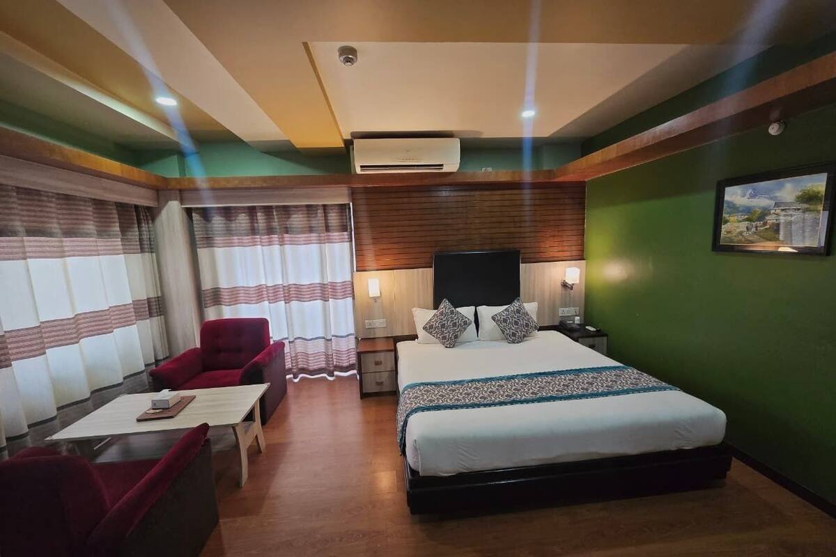 Ein Hotelzimmer mit einem großen Bett, einem roten Sessel, einem Holztisch und einem Fernseher auf einem Holzschrank.