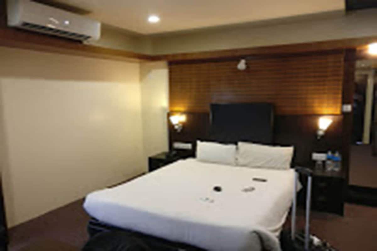 Ein Hotelzimmer mit Bett, Fernseher, Nachttisch und Wandklimaanlage.