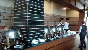 A buffet setup with multiple serving stations, a brick wall, and a polished floor. - Hotel Samana (Hetauda)