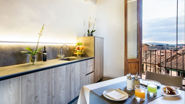 A modern kitchen with a wooden countertop, a sink, and a dining area with a table set for two. - B&B Il Barbero (Siena)