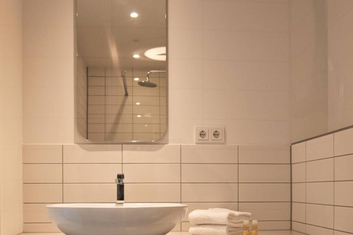 Une salle de bain moderne avec un grand lavabo sur colonne, un miroir, des toilettes et un porte-serviettes.
