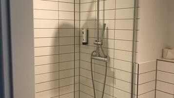 En dusch med ett duschmunstycke som kan hållas i handen och ett fast monterat duschmunstycke, en handduk som hänger på väggen och en hållare för toalettpapper.