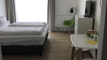 Habitación de hotel con cama, escritorio, silla, televisión y ventana con cortinas.