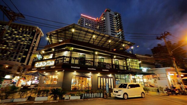 A multi-story building with a restaurant on the ground floor, a car parked in front, and a taller building in the background. - Uno Chiangmai (Chiang Mai)