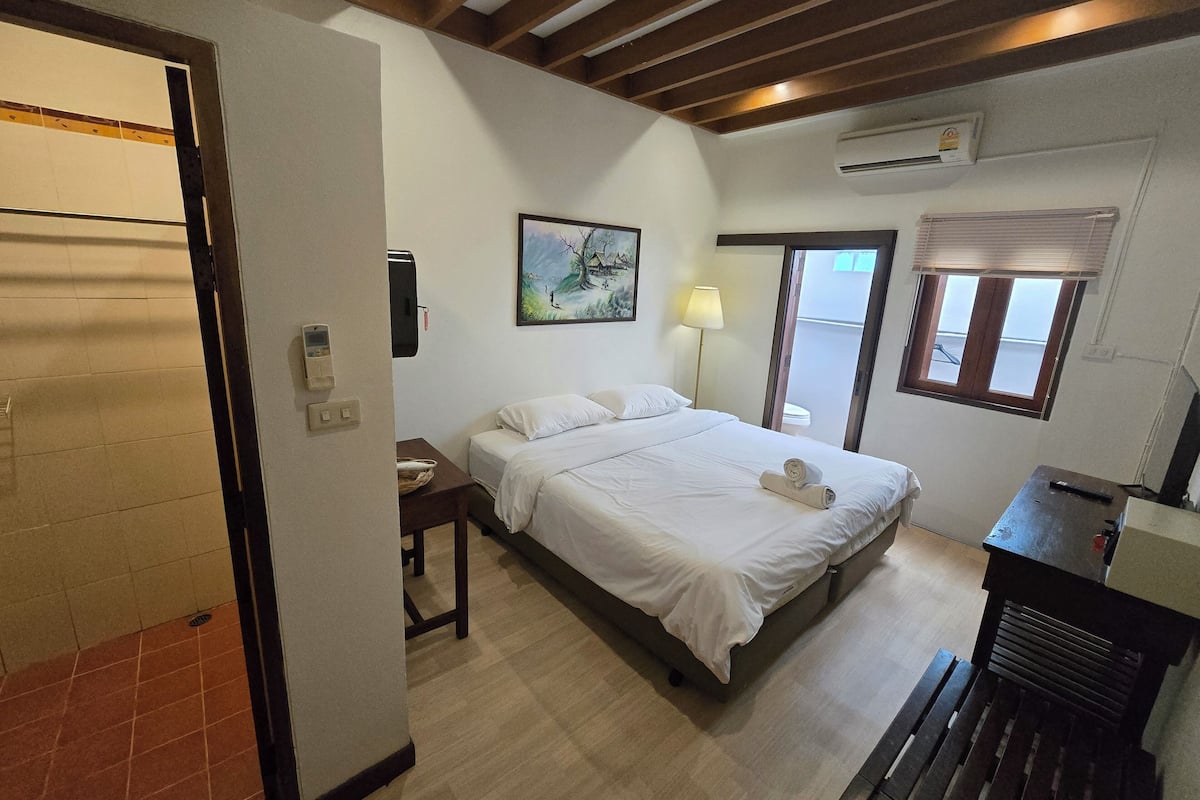 Un dormitorio con cama, mesita de noche, lámpara y un cuadro en la pared.