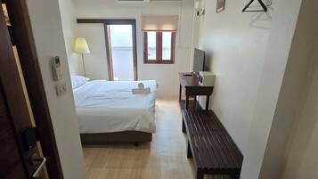 Ein Hotelzimmer mit Bett, Nachttisch, Lampe, Fenster und einer hölzernen Bank.