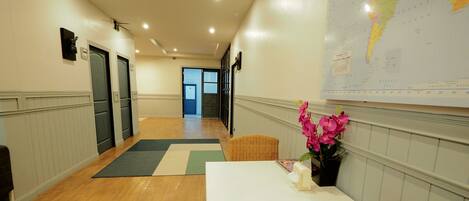 A hotel corridor with a wooden floor, a white table with a vase of flowers, wicker chairs, and a map on the wall.