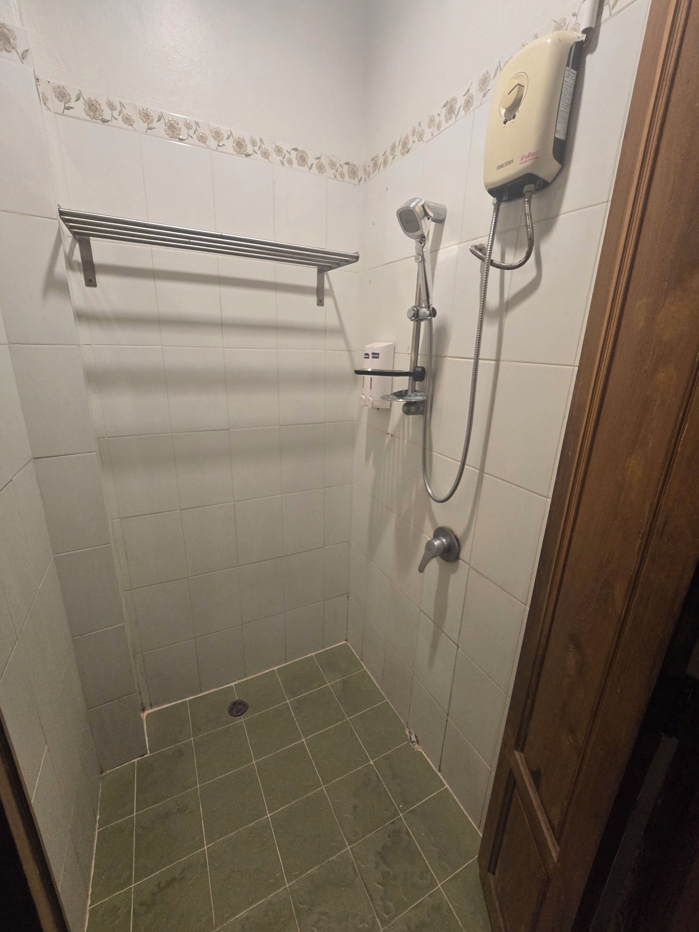 Un baño pequeño con revestimiento de azulejos, ducha de mano, grifo empotrado en la pared y un estante sobre la ducha.