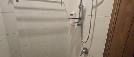 Un baño pequeño con revestimiento de azulejos, ducha de mano, grifo empotrado en la pared y un estante sobre la ducha.