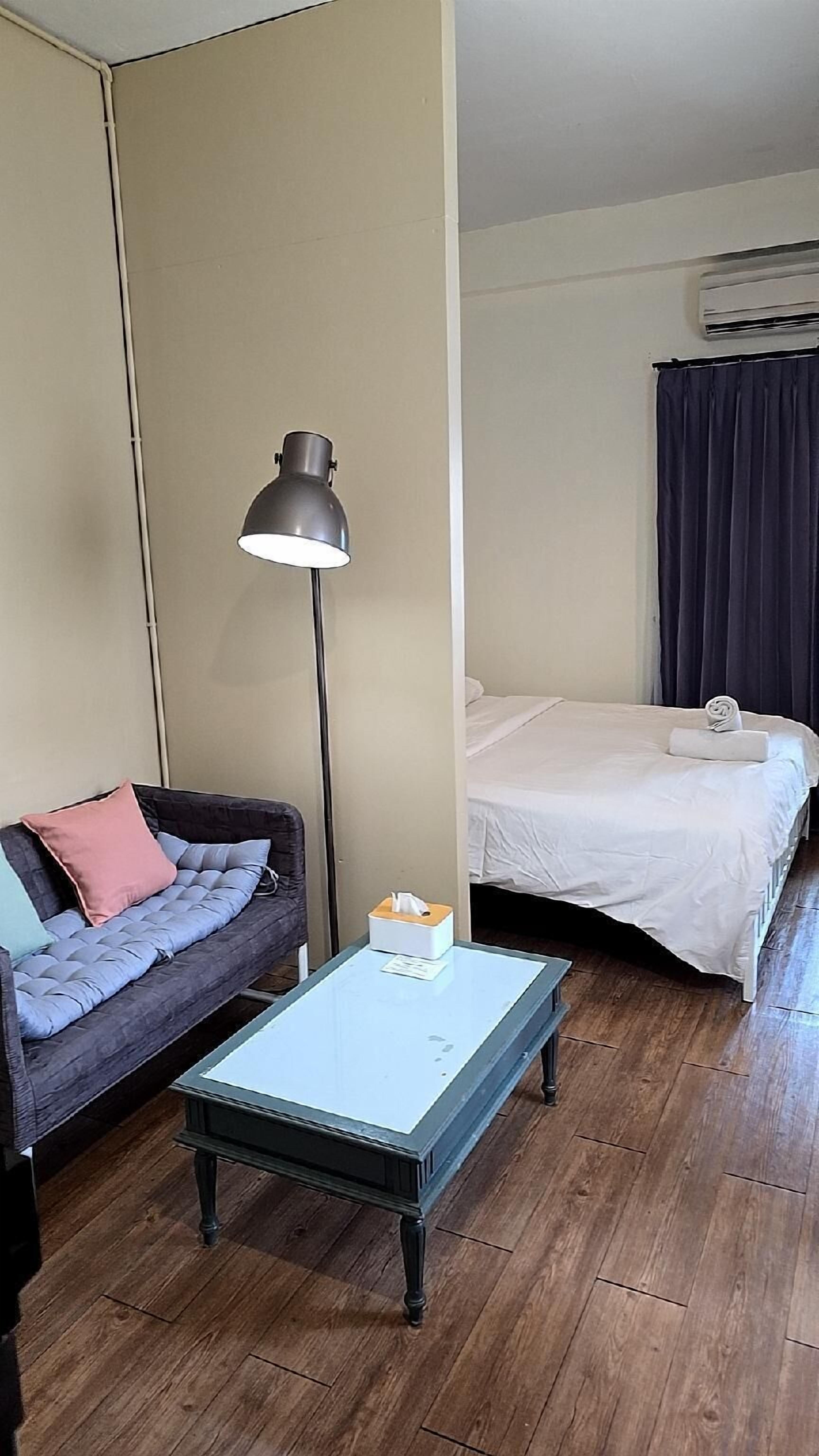 A hotel room with a sofa, a small table, a bed, and a floor lamp.