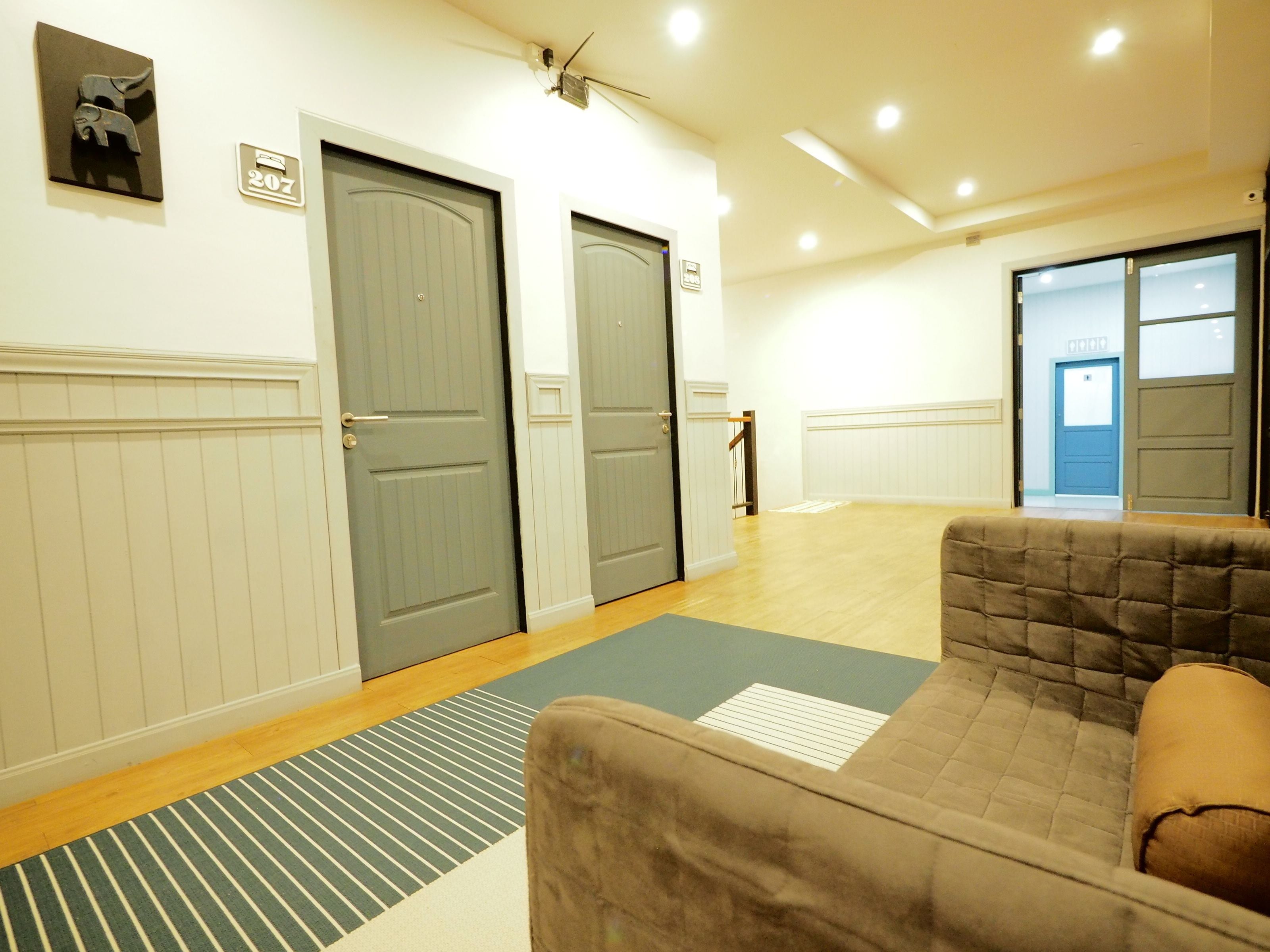 A hotel room with a large window, a sofa, a striped rug, and a door with a number sign.