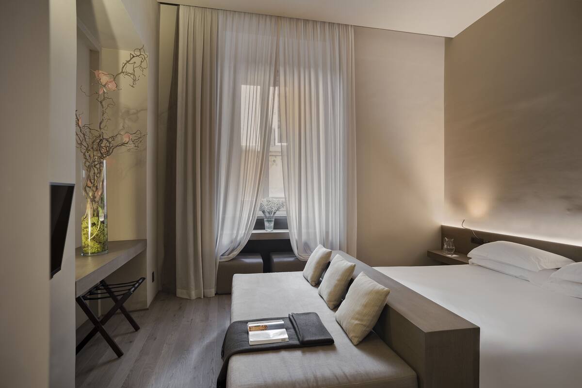 A modern hotel room with a bed, bedside table, and a desk with a chair.