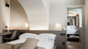 Una habitación de hotel moderna con cama, escritorio y baño con espejo y lavamanos.