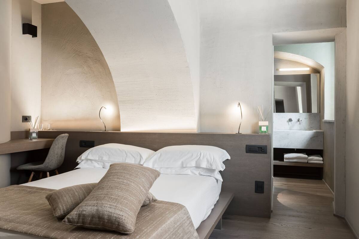 A modern hotel room with a bed, a desk, and a bathroom with a mirror and sink.