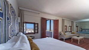A hotel room with a large bed, a sofa, a small table, and a view of the sea through open doors. - Maris Lindos, Suites and Apartments (Rhodes)