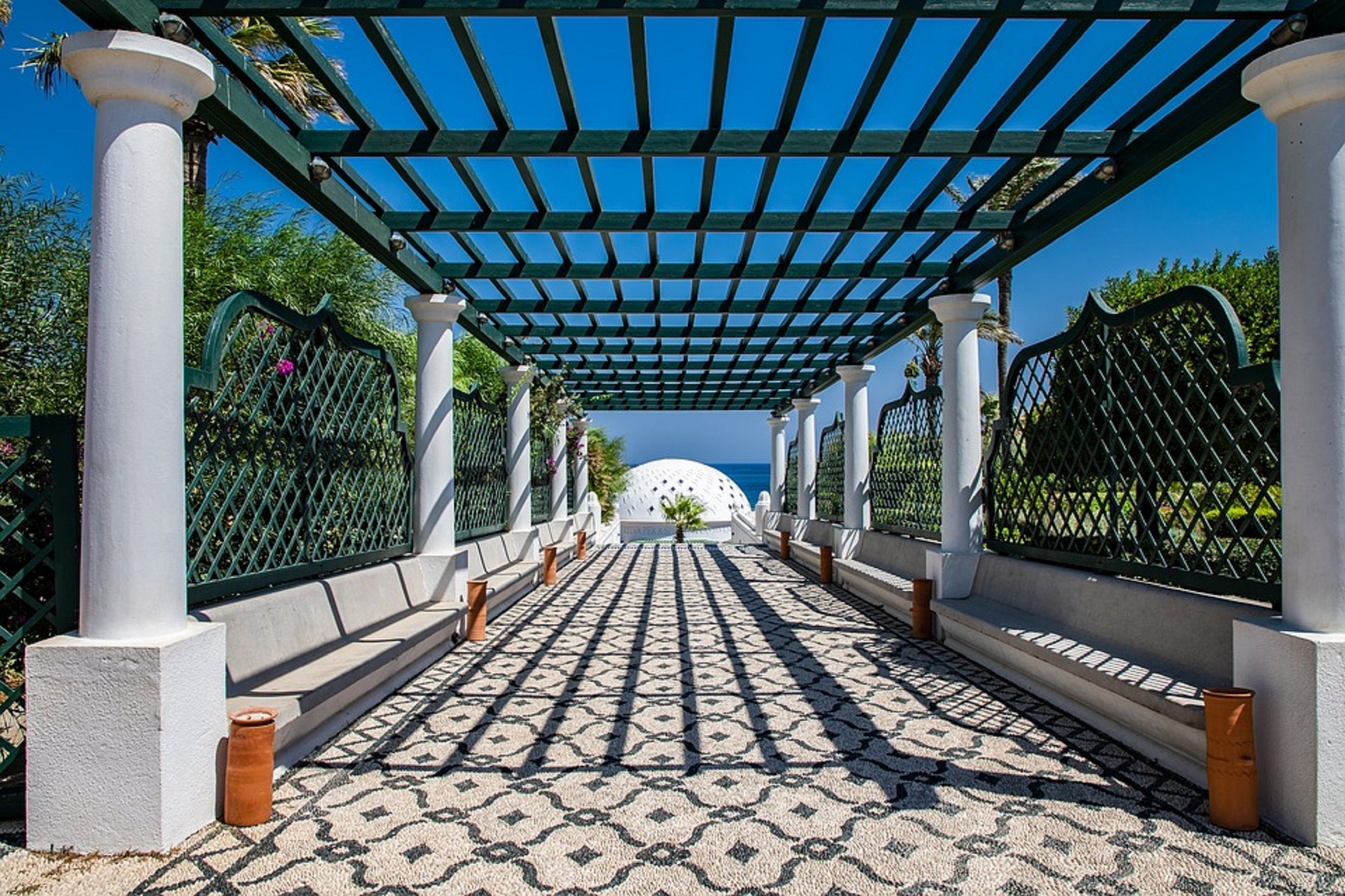 Un pasillo cubierto con piso estampado, columnas blancas y barandillas de metal verde.