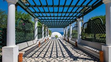 Un pasillo cubierto con piso estampado, columnas blancas y barandillas de metal verde.
